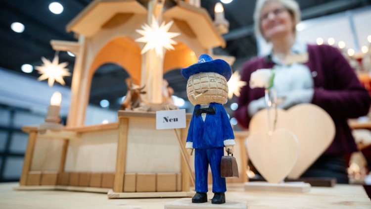 Im Vordergrund ist das geschnitzte Leipziger Messemännchen zu sehen, im Hintergrund sind – leicht verblasst – weitere Holzfiguren sowie die Ausstellerin auf der HANDWERK live zu erkennen.