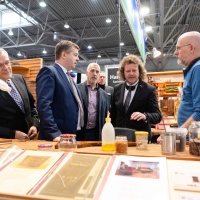 Eine Gruppe an Männern in Anzügen wird von einem anderen Mann an einem Stand beraten.