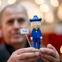 Ein Mann zeigt ein Miniatur Messemänchen in die Kamera.