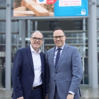 2 Männer in Anzügen stehen vor einem Banner der Handwerksmesse 2026.